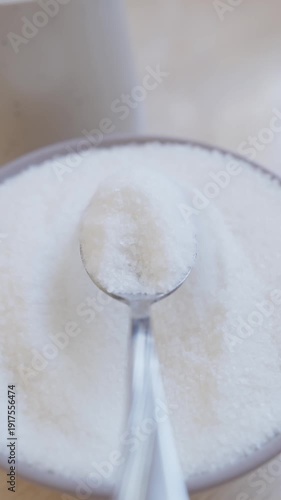 Spoon puts sugar into mug. Sugar spoon glimmers showcasing beauty of this sweet ingredient. From sugar container to bowl. Scoop sugar with spoon and pour it into cup. Vertical video. POV