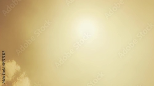 Golden light from a visible sun radiates across a soft sky with delicate clouds, creating a bright and warm atmospheric background for various design needs