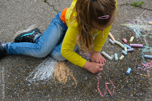 Child paints outdoors. Little girl drawing colored chalk on the asphalt . Creative development of children