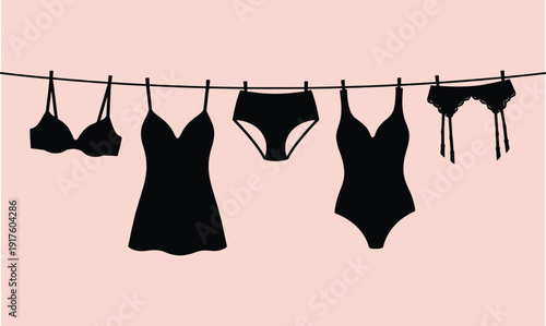 Stylish black lingerie and swimwear collection hanging on a clothesline against a soft pink background