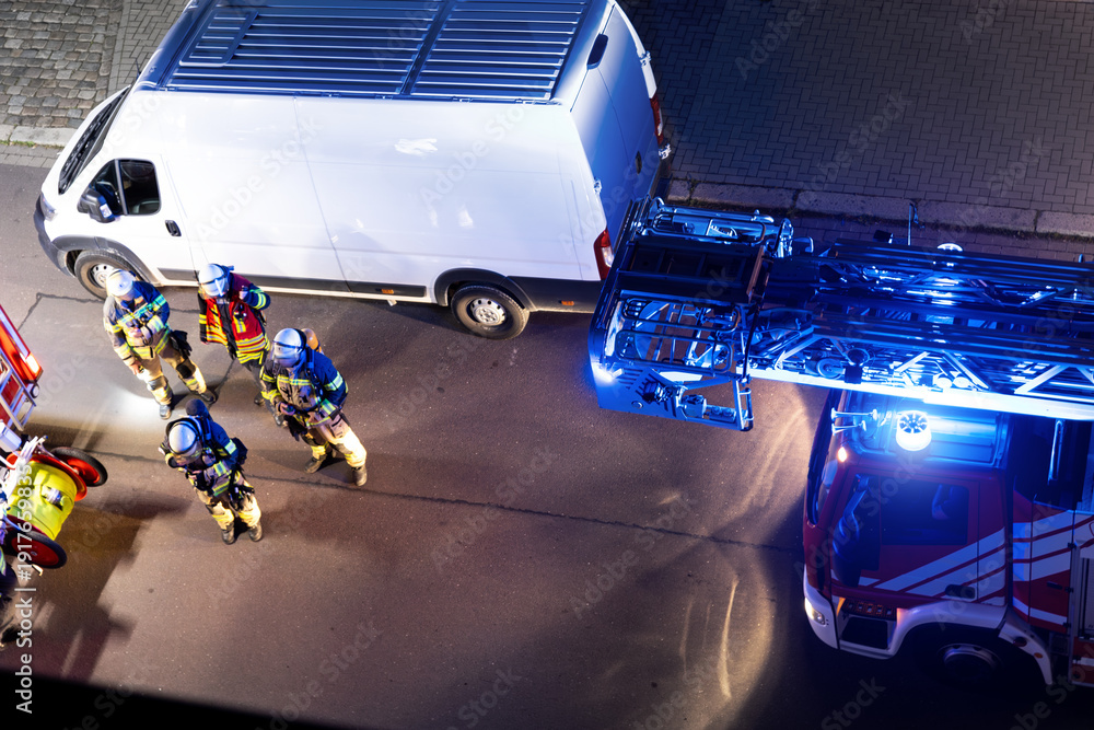 Fototapeta premium Top above view fire engine trucks brigade firefighters ladder and safety equipment at accident highrise tower residential apartment or office building in city center night. Emergency rescue disaster