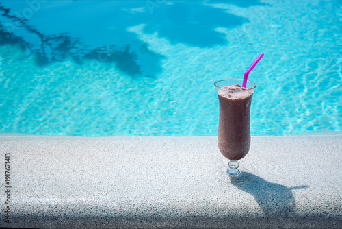 Fotografie Chocolate smoothie in a tall glass with a pink straw placed on a stone ledge bes