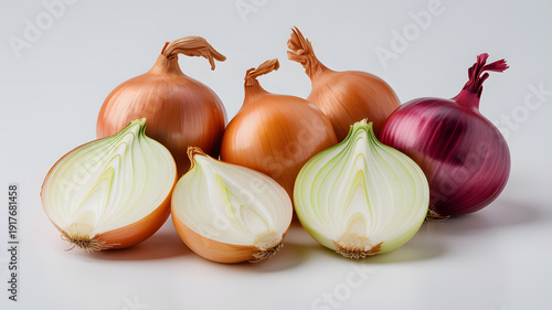 A group of onions and shallots on a white surface, some cut open to reveal their inner layers.