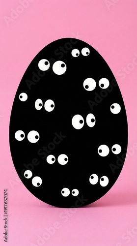 Black easter egg with playful googly eyes on pink background, quirky holiday decor for spring celebration, minimal studio still for party invites and kid crafts