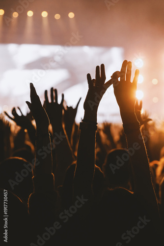 Silhouetted crowd raising hands and rock signs at concert