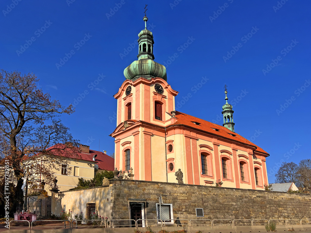 Naklejka premium Church of All Saints in Europe in Prague. Roman Catholic parish with a statue of Jesus on the cross by a tree and part of the castle on the left in the background.