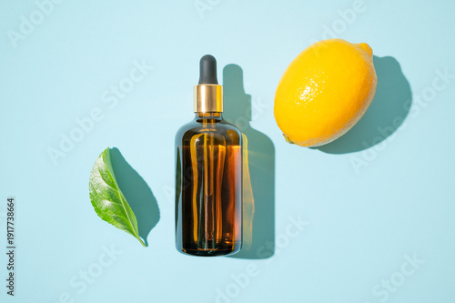 Vitamin C facial serum or essential oil, fresh lemons, green leaves on blue background flat lay top view. Glass bottles with dropper. Natural organic cosmetics. Anti-aging care with antioxidants