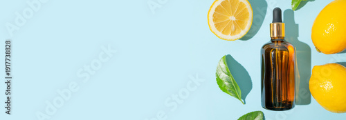 Vitamin C facial serum or essential oil, fresh lemons, green leaves on blue background flat lay top view. Glass bottles with dropper. Natural organic cosmetics. Anti-aging care with antioxidants
