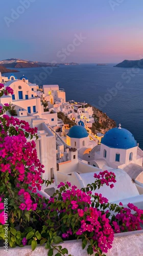 Beautiful panoramic view of white houses with blue domes and vibrant pink bougainvillea flowers at sunset in Oia village, Santorini island, Greece
