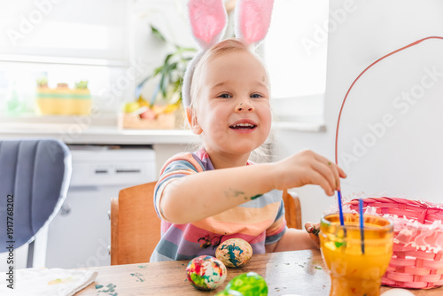 Картината върху платно Happy child with bunny ears celebrating Easter at home while enjoying colorful e