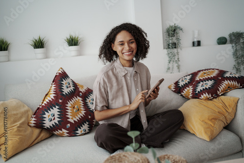 Relaxed Woman Teaching With Smartphone In Cozy Setting Surrounded By Greenery And Soft Cushions