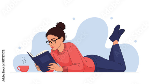 Relaxed young woman with glasses lying on the floor reading an interesting book while enjoying a hot cup of coffee in a peaceful home atmosphere.