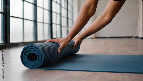 In a serene yoga studio filled with soft light, hands gently roll out a blue mat, preparing for a calming session of mindfulness and movement. Peace envelops the space, inviting focus