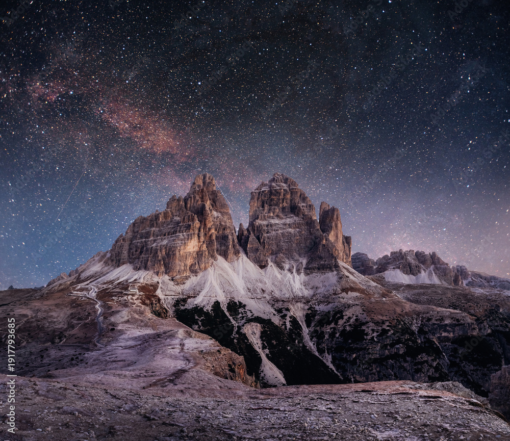 Obraz premium Nighttime alpine landscape with rugged mountain peaks silhouetted against a vivid Milky Way and starry sky, evoking solitude, adventure, and cosmic wonder in a remote high‑altitude setting.
