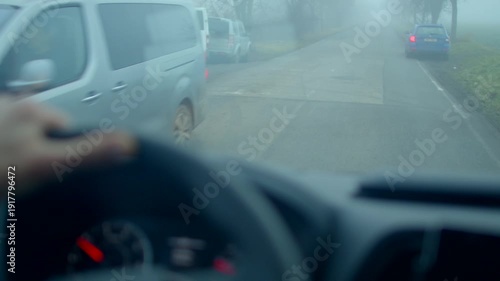 driver pov on foggy road with approaching headlights and railroad crossing, steering wheel grip visible, blurred dashboard, damp asphalt and low visibility creating tense morning commute 