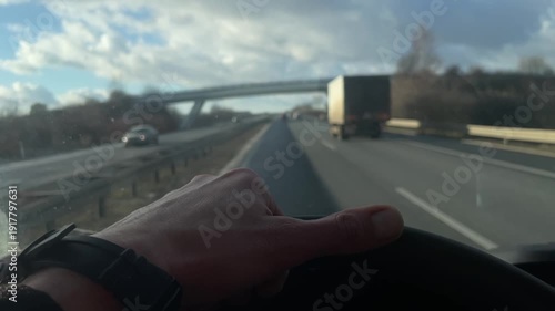 Closeup of commercial driver steering wheel, Focused male commercial driver maneuvering fast lane changes, Closeup of male professional driver handling steering wheel at high speed under cloudy sky 