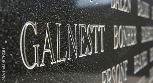 Close up of engraved names on a polished black granite monument, likely a memorial or headstone, with a shallow depth of field