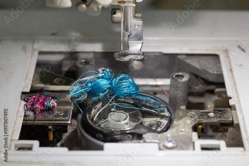 Tangled blue thread mess in embroidery machine bobbin case, mechanical failure and repair concept.