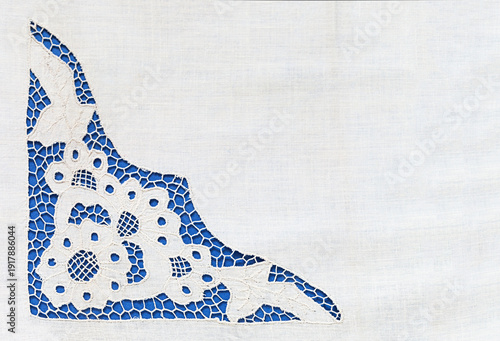 Fragment of white tablecloth with openwork lace embroidery in Richelieu style with cut-out fragments on blue background. Empty space for text. Close-up, top view, copy space, flat lay, blank, mockup