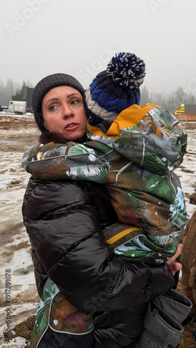 A woman with a child in her arms and emotions on her face in winter, military conflict, refugees.