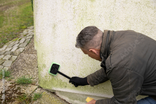 Man inspects and cleans mold and moss on facade with a sponge
