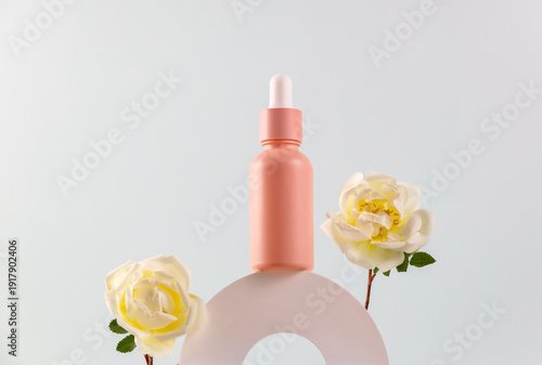 bottle of essential oil with a pipette and cream rose flowers on a white round podium. The concept of skin care using natural cosmetics