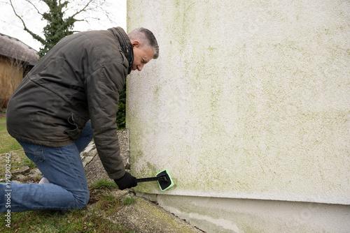 Man inspects and cleans mold and moss on facade with a sponge