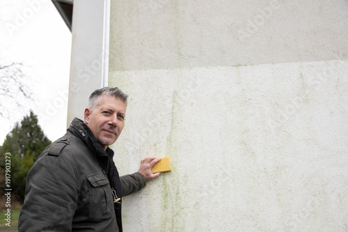Man inspects and cleans mold and moss on facade with a sponge