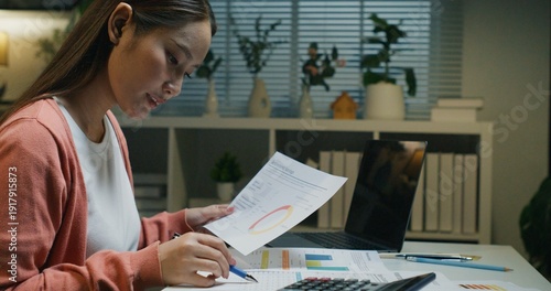 Фотография Late night financial planning scene: An Asian woman analyzing investment data, retirement information, and earning potential to ensure future wealth and a stable economy