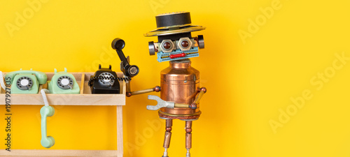 Tableau sur toile Robot operator standing near wooden table with vintage telephones, holding black rotary phone receiver