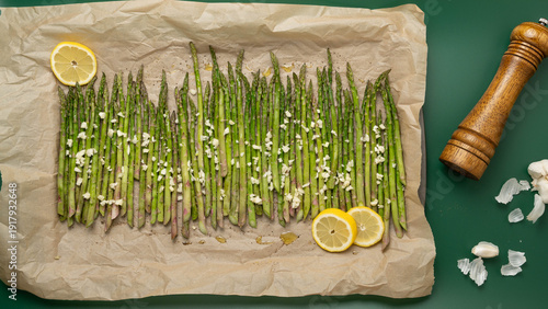 Bild auf Leinwand Raw asparagus drizzled with olive oil, fresh chopped garlic, ground pepper, lemon slices on a parchment paper lined baking sheet