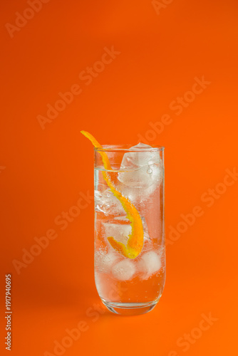 An iced cocktail with a twist of orange peel in a Hi Ball Glass against an orange background