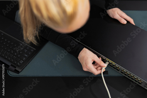 Photography Woman in her 30s with blond hair installs Ethernet cable to network switch in a