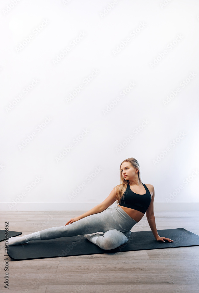 Fototapeta premium Young Woman Stretches Her Body While Practicing Yoga In Activewear At Home For Fitness. Girl Stretching, Enjoying Fitness Training Yoga And Healthy Lifestyle