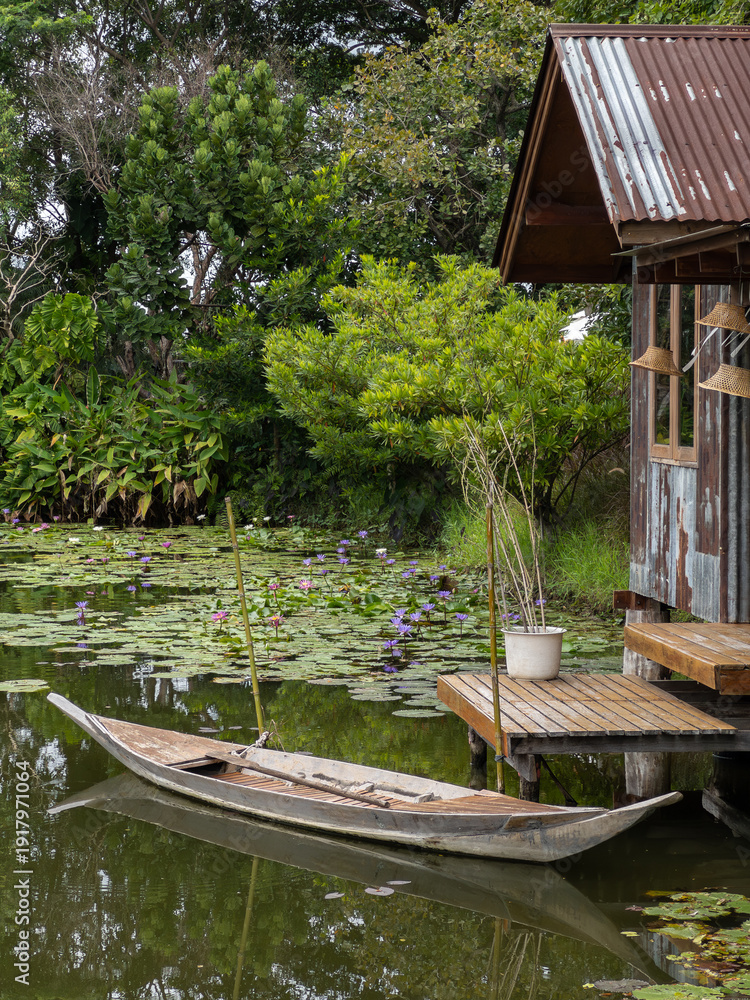 Obraz premium Wooden Rowboat by Rustic Riverside Hut in Lotus Pond.