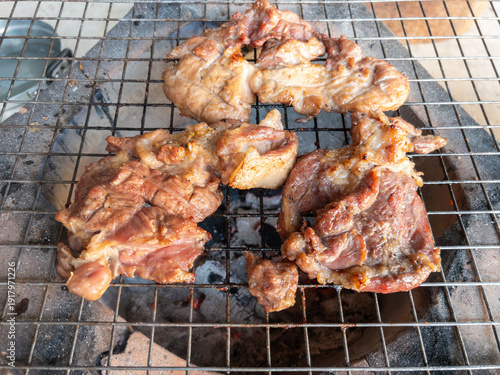 The marinated pork neck meat grilling on a traditional charcoal stove.