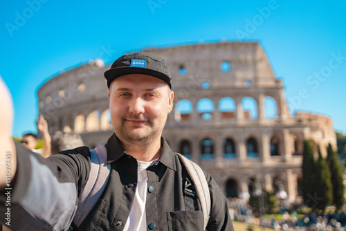 Handsome 30s tourist visiting Colosseum in Rome, Italy. Young man taking photo in front of famous Italian landmark. Travel and holidays concept. High quality photo