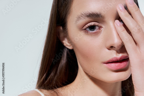 Young woman with captivating eyes gently touching her face in a serene setting