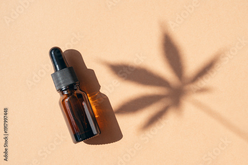 Medical uses of cannabis oil in amber glass dropper bottle on beige background with shadow of leaf
