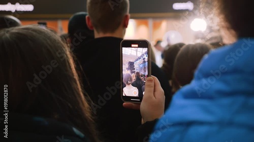 Young fans filming a concert on smartphones in a mall atrium. A huge crowd of teenagers gathered near the stage. Energetic audience enjoying a concert at a public event.