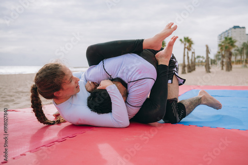 Two people grappling jiu jitsu on beach mat