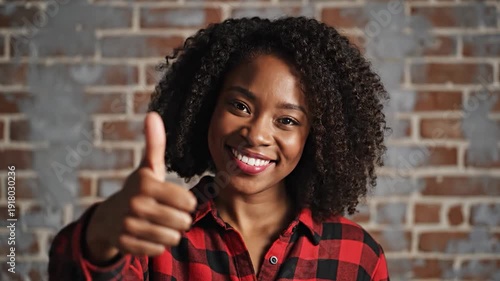 Smiling young woman with curly hair gives a positive thumbs-up gesture against