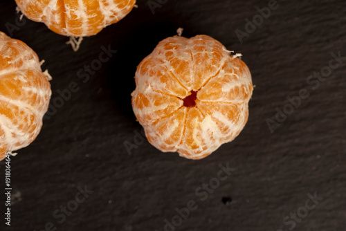 a juicy orange-colored peeled tangerine on a black slate table, a ripe orange small mandarin without a peel on a black slate board