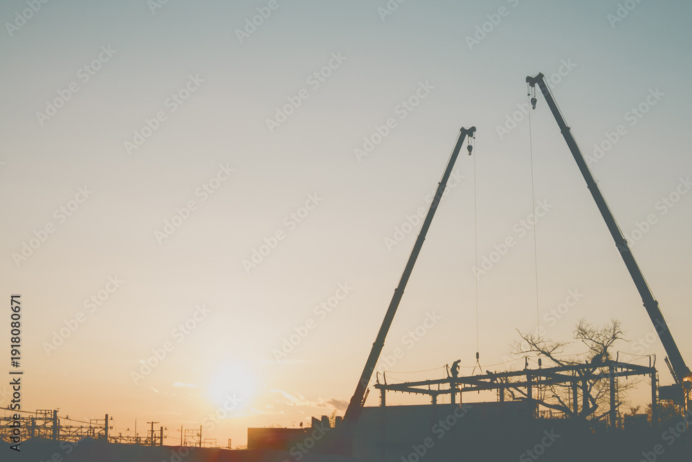 Obraz premium Silhouette of construction cranes, workers, and an overhead railway at sunset.