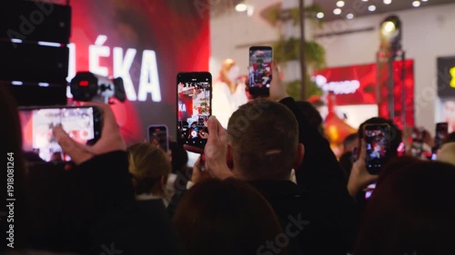 Young fans filming a concert on smartphones in a mall atrium. A huge crowd of teenagers gathered near the stage. Energetic audience enjoying a concert at a public event.