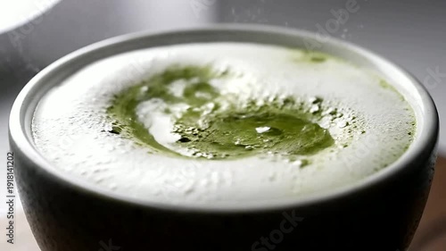 Close up of green liquid pouring in white cream in bowl or Close up of green liquid mixing in white cream in bowl