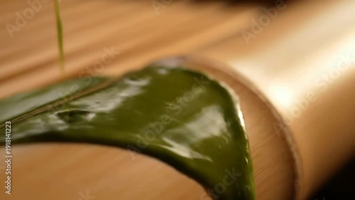 Close up of green liquid pouring onto leaf on wood or Macro of green liquid falling on leaf near bamboo mat