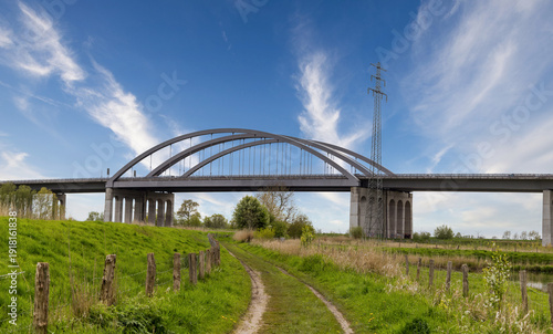 Modern highway arch bridge spanning the Stör River near Itzehoe, Schleswig-Holstein, Germany, under bright blue sky.