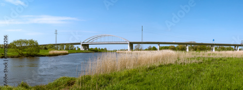 Modern highway arch bridge spanning the Stör River near Itzehoe, Schleswig-Holstein, Germany, under bright blue sky.