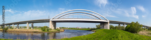 Modern highway arch bridge spanning the Stör River near Itzehoe, Schleswig-Holstein, Germany, under bright blue sky.